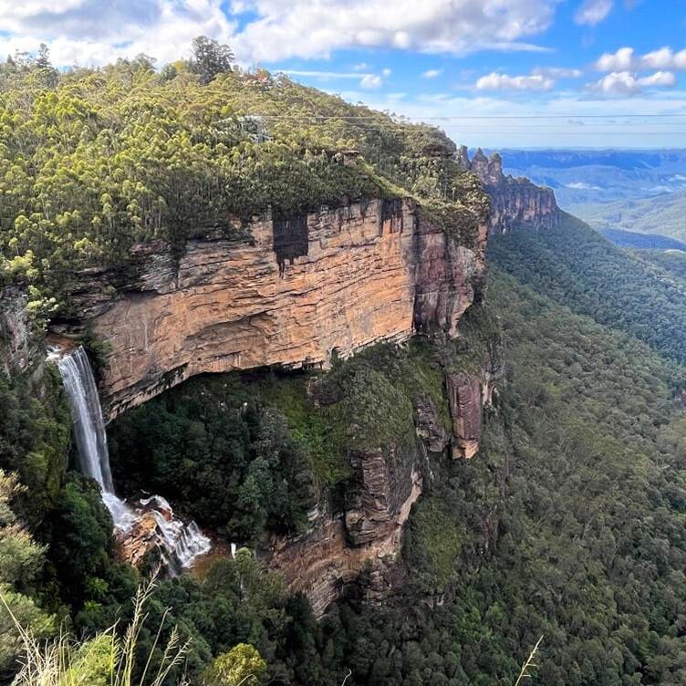 Waterfall plunging beside a forested Blue Mountains sandstone cliff